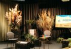 Pasākuma skatuves iekārtojums - diziana klubkrēsli, puķupodi ar dzīviem augiem un augsti žāvēto augu kārtojumi