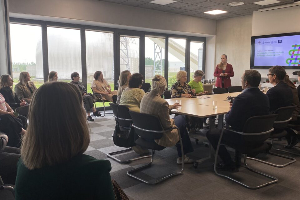 Vairāki cilvēki skatās prezentāciju ar runātāju priekšā.