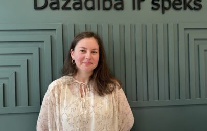 Karolīna Auziņa, SIF eksperte dažādības vadības jautājumos, pie sienas ar uzrakstu “Dažādībā ir spēks”.