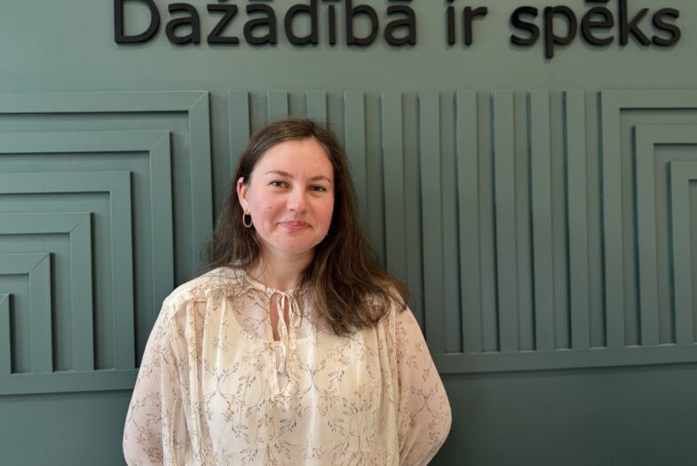 Karolīna Auziņa, SIF eksperte dažādības vadības jautājumos, pie sienas ar uzrakstu “Dažādībā ir spēks”.