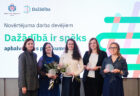Grupas foto ar “Dažādībā ir spēks” apbalvojuma saņēmējiem, kuri tur balvas un ziedus pasākuma norises telpā.
